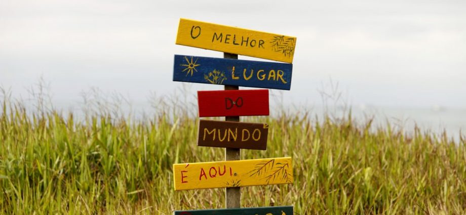 Vibrant multilingual sign in a grassy field in Guaratuba, Paraná, Brazil, showcasing local charm.